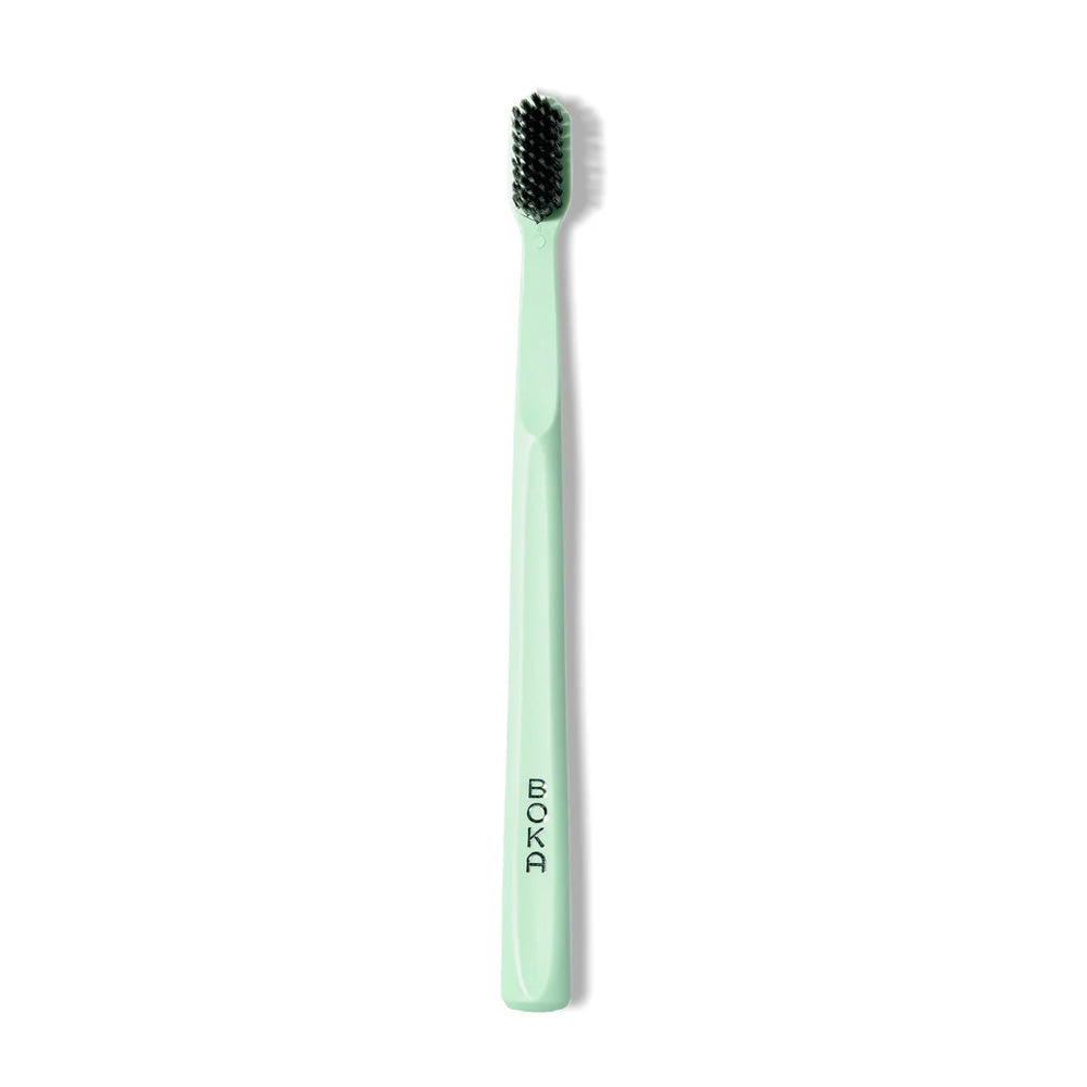 The Classic Toothbrush by BOKA in mint green features black charcoal bristles for a gentle clean.
