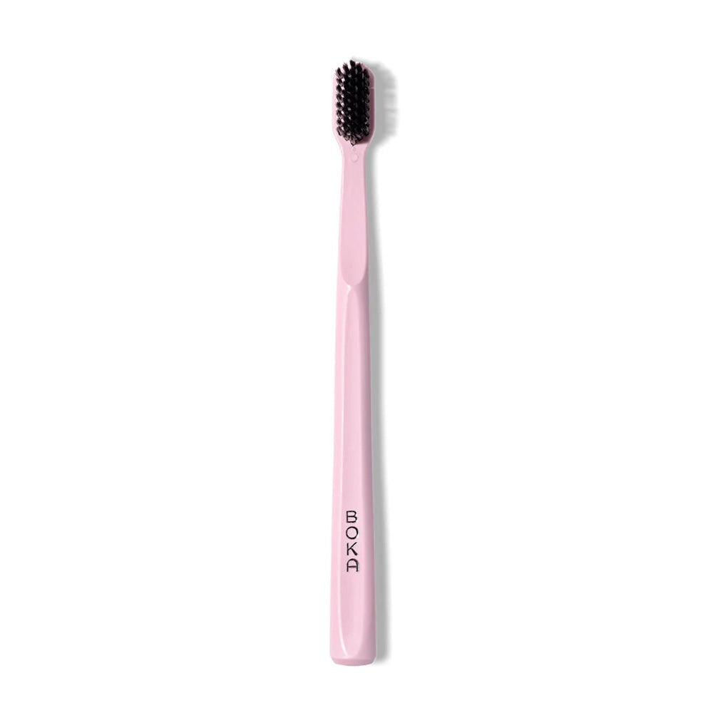 The Classic Toothbrush has pink bristles with activated charcoal and BOKA printed on the handle.